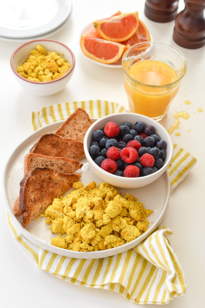 A breakfast table with a a plate of scrambled tofu scrambled eggs and a slice of toast with berries.