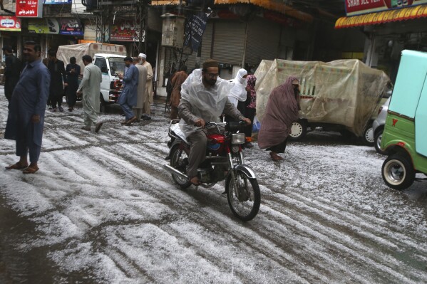 People walk on the road covered by hailstones due to heavy hailstones rain in Peshawar, Pakistan, Saturday, March 30, 2024. Heavy rains killed eight people, mostly children, and injured 12 in Pakistan's northwest, an official said Saturday. (AP Photo/Mohammad Sajjad)