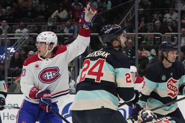Montreal Canadiens left wing Juraj Slafkovsky, left, reacts to the goal from teammate defenseman Kaiden Guhle as Seattle Kraken defenseman Jamie Oleksiak (24) and defenseman Will Borgen, right, react during the first period of an NHL hockey game, Sunday, March 24, 2024, in Seattle. (AP Photo/Lindsey Wasson)