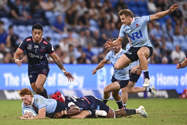 Tane Edmed, bottom left, of the Waratahs is tackled during during the Super Rugby match between the Waratahs and the Rebels in Sydney, Australia, Friday, March 29, 2024. (James Gourley/AAP via AP)