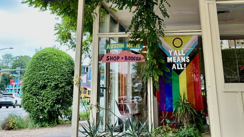 the window of austin motel with a pride flag that says "y'all means all!"