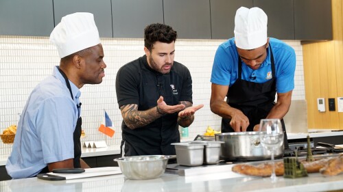 David Robinson and his son Corey Robinson flank Kévin D'Andrea in a white kitchen over a stovetop.
