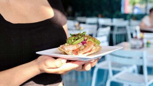 A woman holding a shrimp tostada on a a square white plate.
