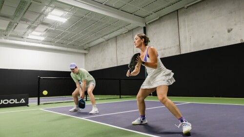 Two people playing doubles on one side of the indoor court, which is purple and green.