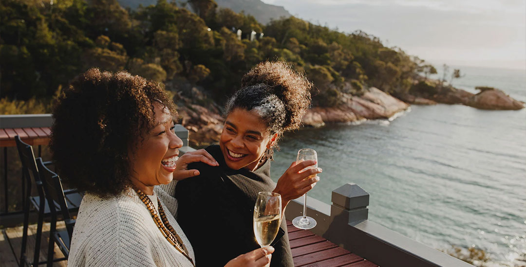 Immersive Experiences slider image of 2 women laughing and holding a glass of champagne on a patio