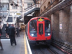 A red S7 Stock train arriving at the clockwise platform at Aldgate station, with passengers waiting to board