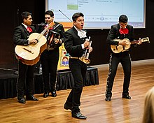 A student mariachi band plays in front of a projected screen
