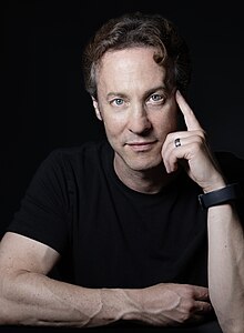 David Eagleman wearing a dark shirt, looking left of camera and appearing to speak