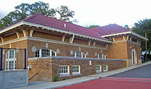 A tan brick railway station building with a red tile roof