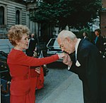 Denis Thatcher, suami mantan Perdana Menteri Britania Raya Margaret Thatcher, mencium tangan Ibu Negara Amerika Serikat Nancy Reagan pada tahun 1988