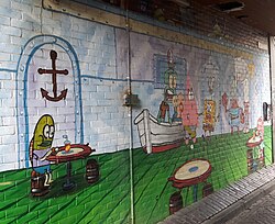 Seinämaalaus, joka esittää Ravun kuori -ravintolan sisäpuolta. Helmi on kuvassa isänsä Johtaja Ravun oikealla puolella.