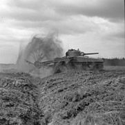 A spinning flail in front of a tank throws dirt into the air