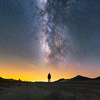 אישה מביטה לאופק ומעליה גלקסיית שביל החלב, במדבר בקליפורניה, ארצות הברית.