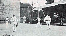 Quatre hommes sur un terrain, l'un s’apprêtant à propulser une pelote à l'aide d'une crosse.