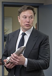 Musk, dressed in a suit, holds a metal model of the Starship