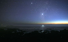Ảnh chụp bầu trời đêm từ bờ biển. Ánh sáng mờ nhạt của Mặt Trời ở phía đường chân trời. Có rất nhiều ngôi sao trên bầu trời. Sao Kim ở giữa, sáng hơn bất kỳ một ngôi sao nào khác, ánh sáng của nó có thể phản chiếu từ mặt đại dương.