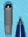 Un impianto standard a forma di radice di 13 mm, con accanto una penna per confrontare le dimensioni