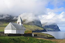 Viðareiðis kirkja med utsikt mot høye klipper.