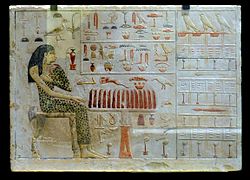Bas-relief peint sur stèle représentant la princesse Nefertiabet face à son repas funéraire et des étoffes qui lui sont offertes, IVe dynastie, Musée du Louvre.