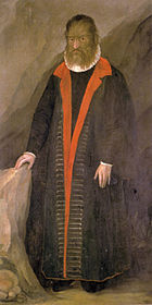 Homem com rosto muito peludo, usa roupas escuras longas e está dentro de uma caverna. Imagem do período medieval.