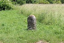 V travnaté ploše stojí kamenný patník s reliéfem.