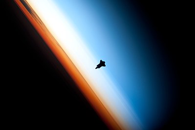 The silhouette of space shuttle Endeavour seen against Earth's colorful horizon during shuttle mission STS-130