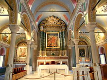 A view of the inside of the cathedral which features high ceilings and colorful walls. There are white pillars and arches throughout. A variety of artwork is displayed on the walls.