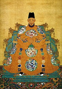 Mladý muž ve slavnostní široké žluté róbě s vyšitými draky v kruzích, s černým turbanem, sedící na trůnu (který za doširoka rozprostřeným oděvem téměř není vidět).
