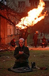 Čečens lasa lūgšanu Pirmās Groznijas kaujas laikā; fonā deg pārrautais gāzesvads