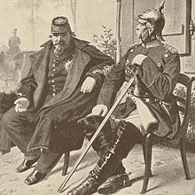 Les deux hommes sont assis côte à côte. Les deux sont en uniformes, Bismarck a un casque à pointe, Napoléon un képi. Alors que Bismarck se tient droit avec le menton haut, Napoléon est avachi sur sa chaise.