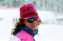 Eine junge Frau mit Mütze und aufgesetzter Sonnenbrille blickt lachend in Richtung der Kamera.