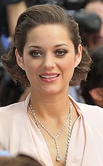Headshot of a brown-haired French female wearing a silver necklace and a pink dress.
