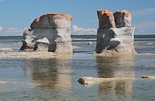 Deux rochers percés par l'érosion se dressent dans une eau peu profonde.