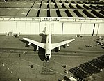 Cliché noir et blanc. Vue supérieure. Avion quadriréacteur sur un tarmac devant des hangars.