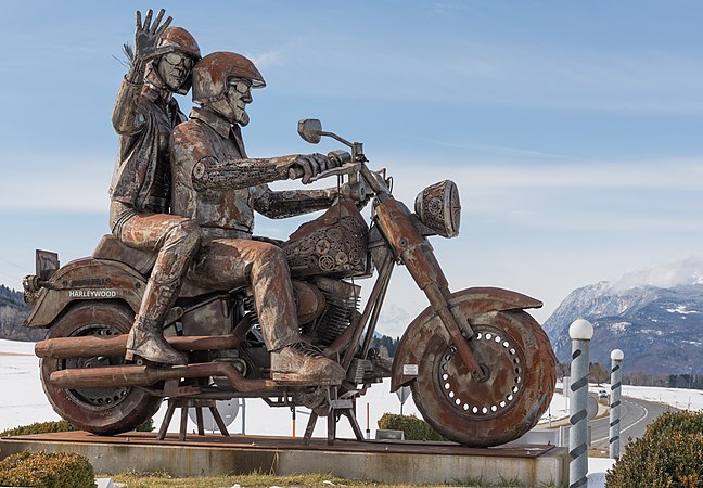 图为一座钢质纪念碑，坐落于奥地利法克湖畔，展现一对夫妇骑乘哈雷Fat Bob摩托车。