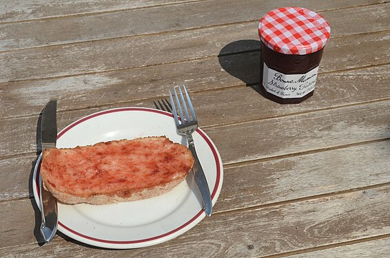 A picnic lunch, featuring strawberry jam on a piece of bread