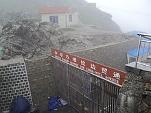 Un passage muré fermé par un portail métallique surmonté d'une double inscription en chinois et en anglais.