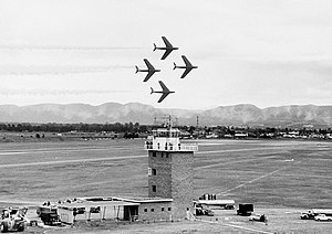 Four single-engined swept-wing jets in a diamond formation above an air base