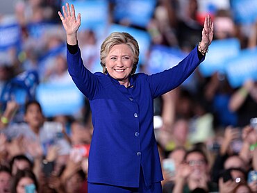 Clinton dalam setelan biru, melihat ke arah kamera. Penonton di latar belakang. Dia adalah di sebuah acara berbicara di Tempe pada 2 November 2016.