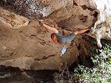 Un grimpeur agrippant dans un toit sur un bloc en extérieur et écartant les jambes pour accrocher ses pieds aux prises