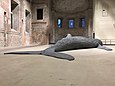Ein Wal liegt in einer kahlen, unverputzten Apsis. Seine Flossen liegen kraftlos auf dem Boden.
