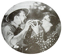 A promotional image showing a woman in a polka-dotted shirt receiving water from a man in a safari hat.