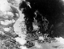 Black and white aerial photograph showing an industrial facility on fire