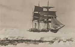 Tre masted skip med seil spredt, omgitt av pakkis, med et smalt kjørefelt vann i forgrunnen