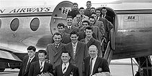 Một bức ảnh đen trắng của một số người trong bộ quần áo và áo khoác trên cầu thang của một chiếc máy bay.