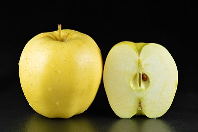 One whole and one halved Golden Delicious apple against a black background