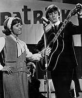 Patty Duke holds a microphone stand for Jeremy as he tunes his guitar