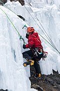 Un grimpeur escaladant une cascade de glace avec piolets et crampons