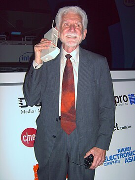 Американский инженер Мартин Купер в 2007 году. В руках одна из первых моделей сотового телефона.