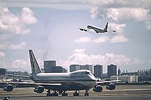 Boeing 747 di landasan pacu dan 707 mengudara